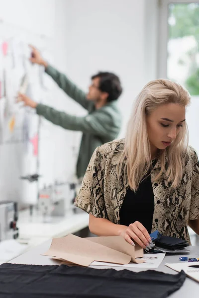 Trendy designer working near color palette, fabric and sewing patterns while colleague working on blurred background — Stock Photo