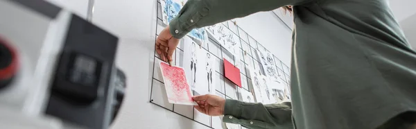 Low angle view of cropped fashion designer attaching drawings on wall in atelier, banner — Stock Photo