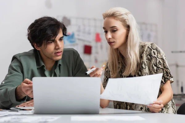 Couple of young designers pointing at laptop while working in fashion atelier — Stock Photo