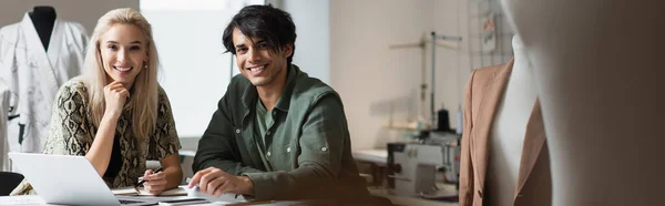 Cheerful fashion designers smiling at camera near laptop and mannequins, banner — Stock Photo