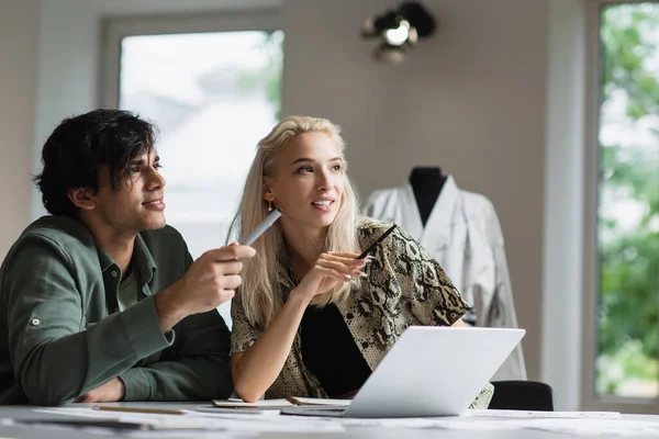 Créateurs de mode positifs souriant tout en pointant du doigt dans le magasin de tailleur — Photo de stock