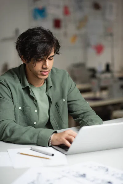 Young fashion designer typing on laptop in tailor shop — Stock Photo