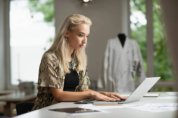 Дизайнер блондинка моди друкує на ноутбуці біля гаджетів на робочому місці — стокове фото