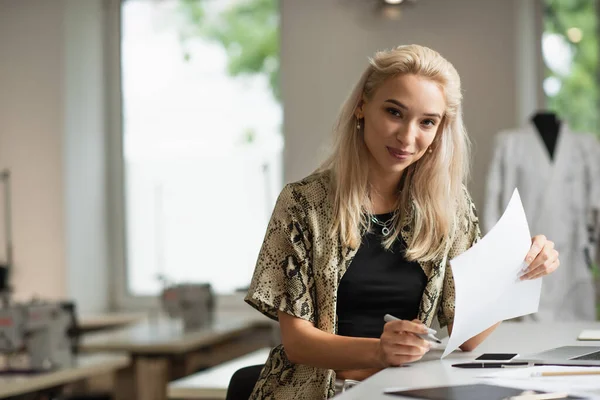 Stylish fashion designer looking at camera while holding document at workplace — Stock Photo