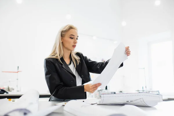 Stylish fashion designer looking at paper at workplace in fashion workshop — Stock Photo