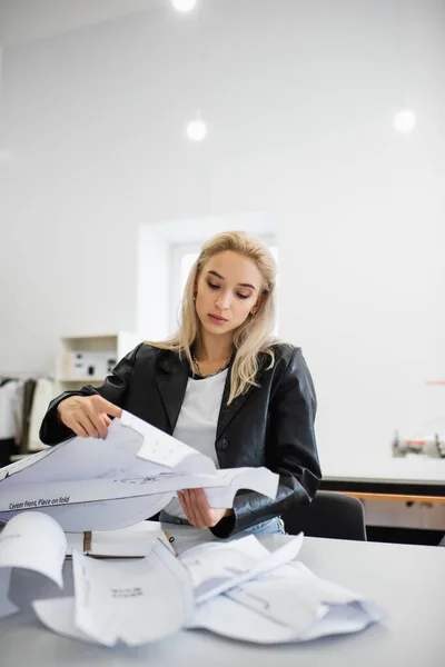 Stylish fashion designer looking at sewing patterns while sitting at workplace — Stock Photo