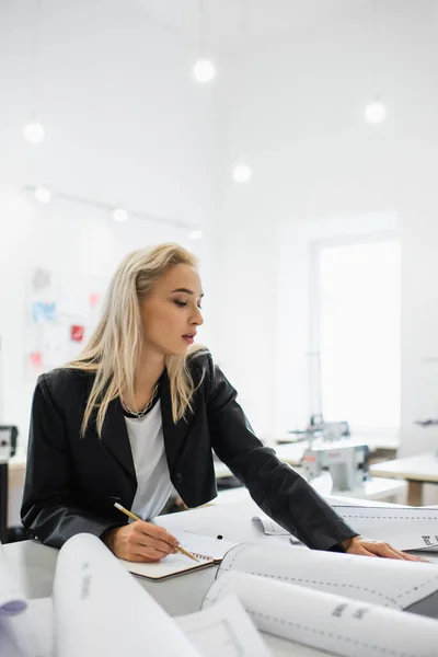 Young fashion designer writing in notebook near sewing patterns in atelier — Stock Photo