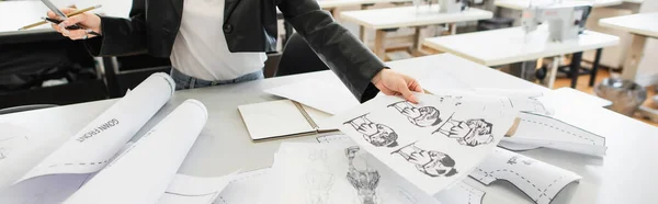 Cropped view of fashion designer sitting near sketches and sewing patterns in atelier, banner — Stock Photo