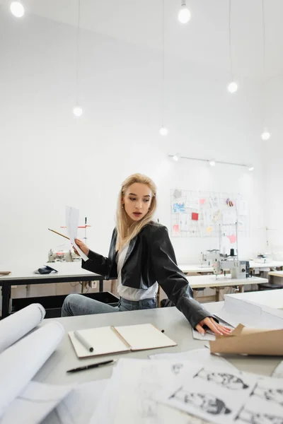 Fashion designer holding paper and pencil while looking at sewing patterns — Stock Photo