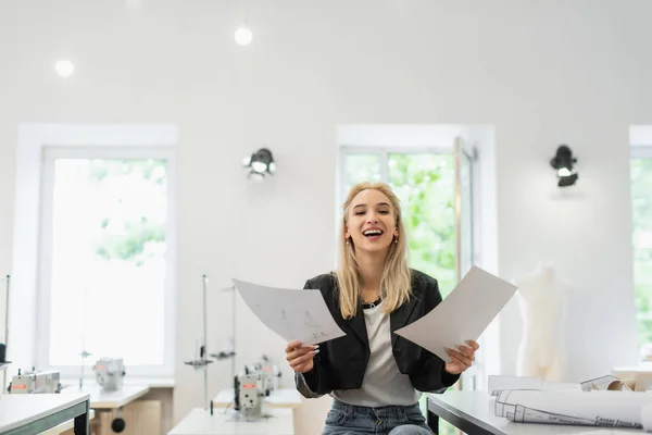 Happy fashion designer smiling at camera while holding sketches — Stock Photo