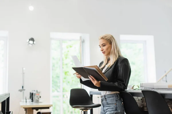 Модний дизайнер стоїть з блокнотом і папером в майстерні моди — Stock Photo