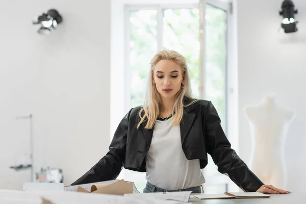 Trendy fashion designer looking at sewing patterns while working in tailor shop — Stock Photo