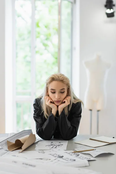 Young fashion designer thinking near sewing patterns and sketches at workplace — Stock Photo