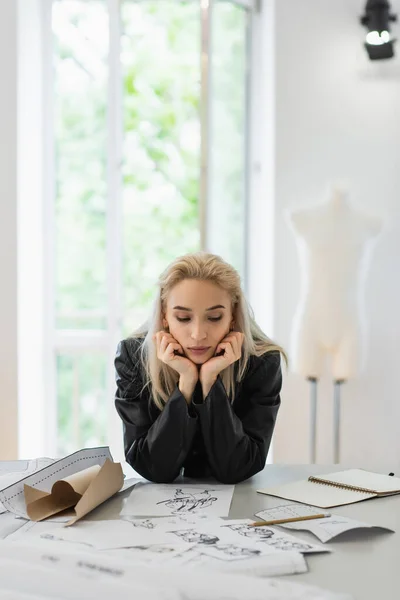 Joven diseñador de moda pensando cerca de patrones de costura y bocetos en el lugar de trabajo - foto de stock