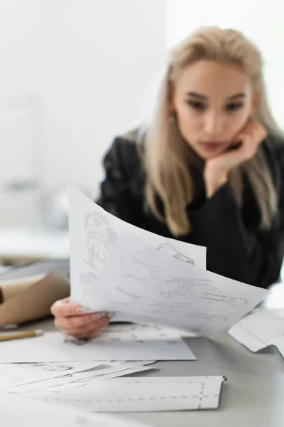 Blurred fashion designer looking at sketches at workplace in tailor shop — Stock Photo