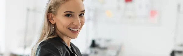 Blonde fashion designer smiling at camera in tailor shop, banner — Stock Photo