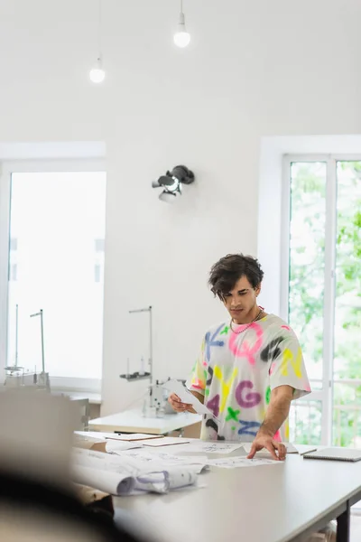 Estilista elegante que trabalha com esboços no atelier da forma, foreground borrado — Fotografia de Stock