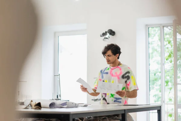 Fashionable designer standing with sketches on blurred foreground — Stock Photo