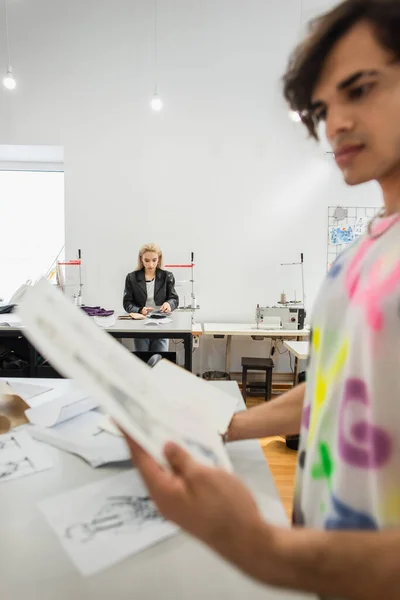 Розмитий дизайнер моди дивиться на малюнок поруч з колегою, що працює на фоні — стокове фото