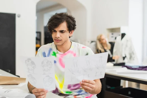 Stylish fashion designer looking at drawings near coworker on blurred background — Stock Photo