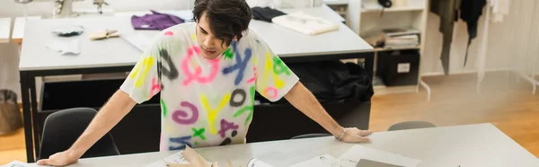 Estiloso designer de pé perto de padrões de costura na mesa na loja de alfaiate, banner — Fotografia de Stock