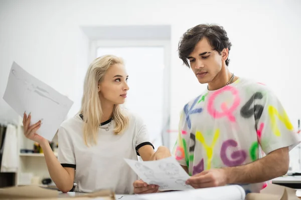 Blonde Designerin zeigt auf Zeichnung, während sie mit Kollegin in Schneiderei arbeitet — Stockfoto