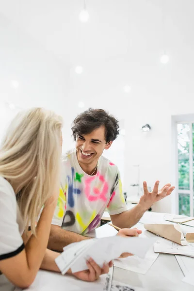 Emocionado diseñador gesto mientras habla con rubia colega en el taller de moda - foto de stock