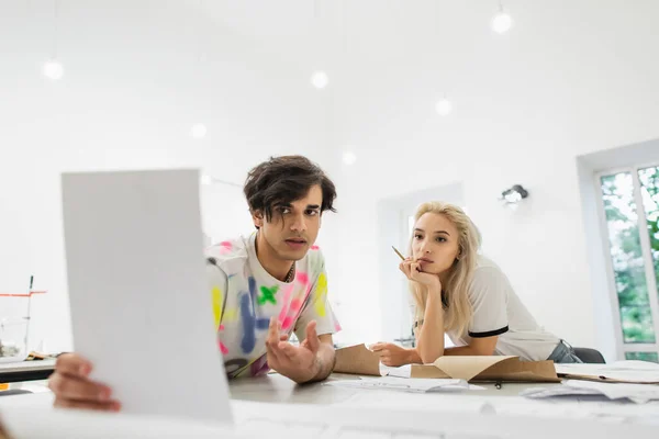 Designer de moda mostrando papel para jovem colega no atelier de moda — Fotografia de Stock