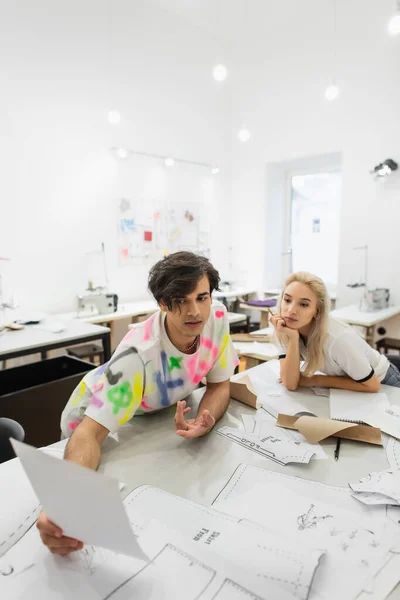 Designer élégant montrant papier à collègue près de modèles de couture — Photo de stock