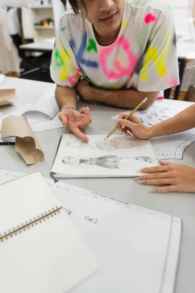 Vista recortada del diseñador apuntando al dibujo cerca de colega sosteniendo el lápiz - foto de stock