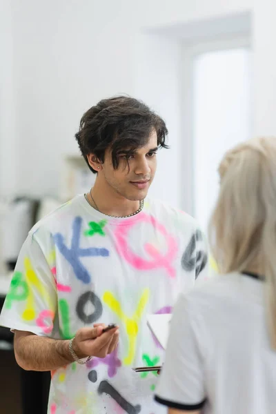 Trendy fashion designer talking to blurred colleague in workshop — Stock Photo