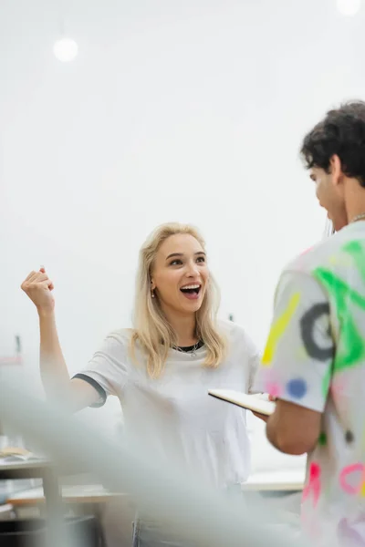 Excited fashion designer showing win gesture near colleague, blurred foreground — Stock Photo