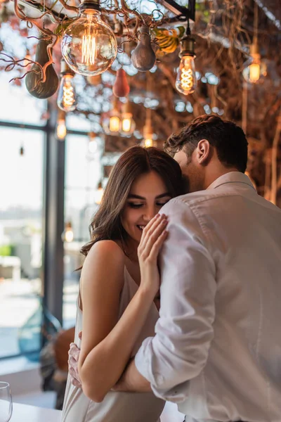 Hombre besar y abrazar alegre joven mujer en restaurante - foto de stock