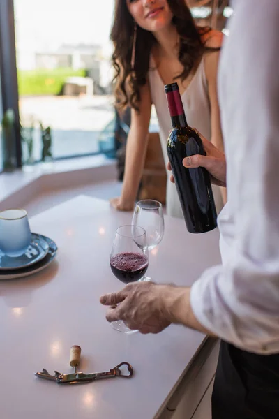 Обрезанный вид мужчины, держащего бутылку красного вина рядом с женщиной в ресторане — стоковое фото