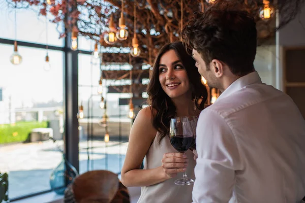 Homem sorridente e mulher segurando copos de vinho tinto no restaurante — Fotografia de Stock