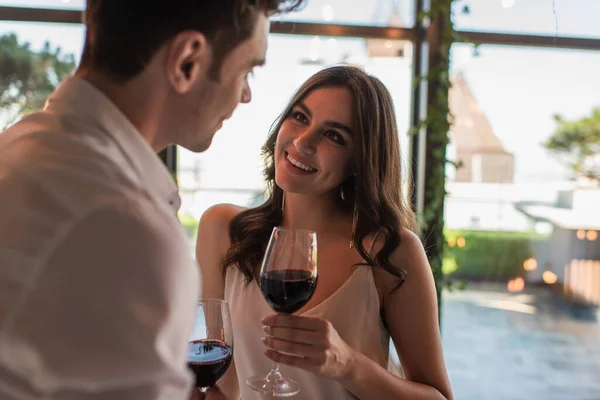 Mulher alegre segurando copo de vinho e olhando para o homem borrado — Fotografia de Stock