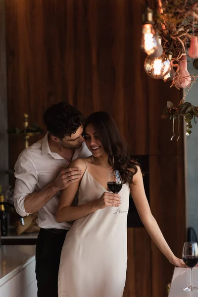 Homem seduzindo mulher sorridente em vestido de deslizamento com copo de vinho — Fotografia de Stock