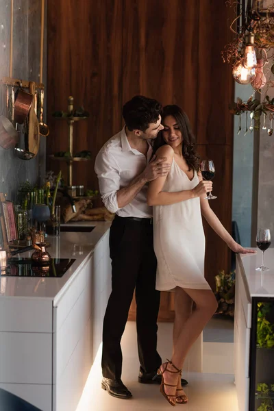 Homem sedutor sorrindo namorada em vestido de deslizamento com copo de vinho — Fotografia de Stock