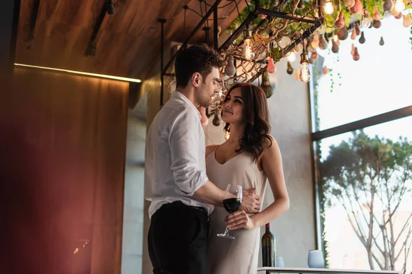Cheerful man hugging joyful girlfriend in slip dress in restaurant — Stock Photo