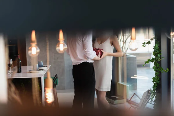 Vista recortada del hombre sosteniendo caja de regalo roja cerca de la novia en vestido de deslizamiento de pie en el restaurante - foto de stock