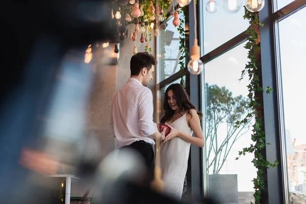 Homme heureux donnant boîte-cadeau rouge à petite amie souriante en robe glissante — Photo de stock