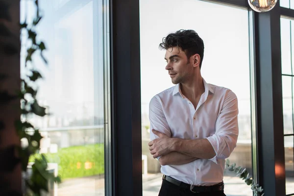 Elegante uomo in camicia bianca in piedi con braccia incrociate vicino alle finestre — Foto stock