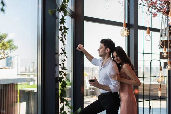 Cheerful young woman hugging elegant man with glass of red wine — Stock Photo