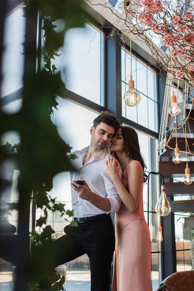 Cheerful young woman hugging pleased man with glass of red wine — Stock Photo