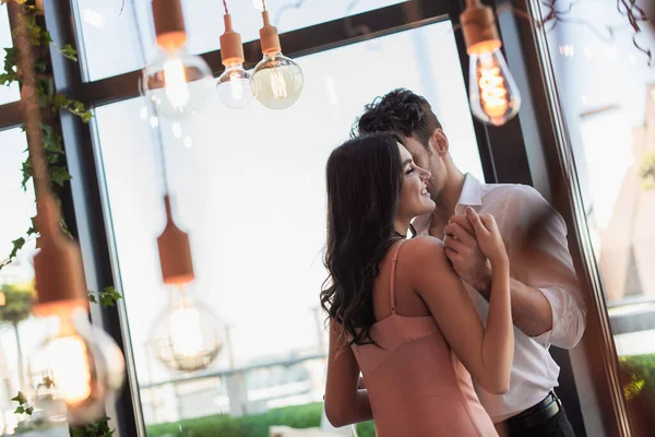 Hombre y mujer feliz tomados de la mano en el restaurante cerca de bombillas decorativas — Stock Photo