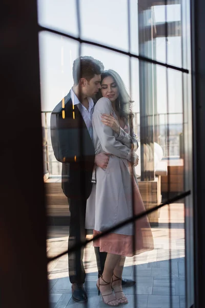 Pareja amorosa abrazándose en la terraza detrás de la ventana borrosa del restaurante - foto de stock