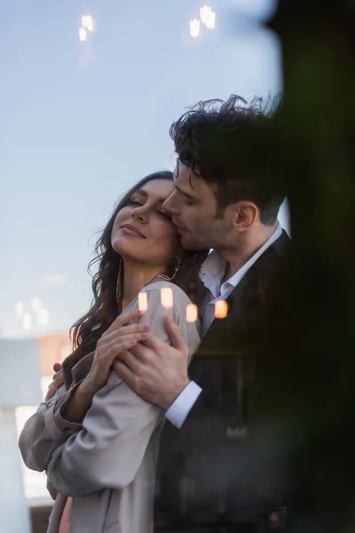 Man hugging happy woman on terrace behind blurred window of restaurant — Stock Photo