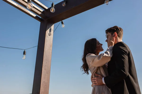 Baixo ângulo de visão do homem e mulher feliz abraçando e olhando um para o outro no terraço do restaurante — Fotografia de Stock