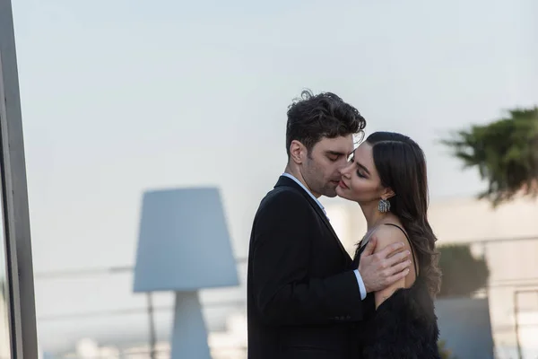 Hombre abrazando sonriente mujer en vestido en terraza del restaurante - foto de stock