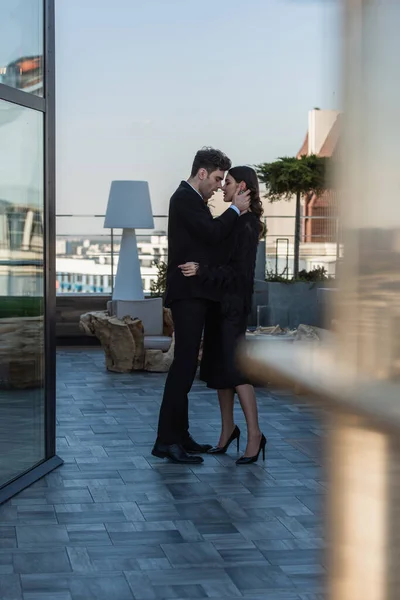 Comprimento total do homem abraçando mulher em vestido preto no terraço do restaurante — Fotografia de Stock